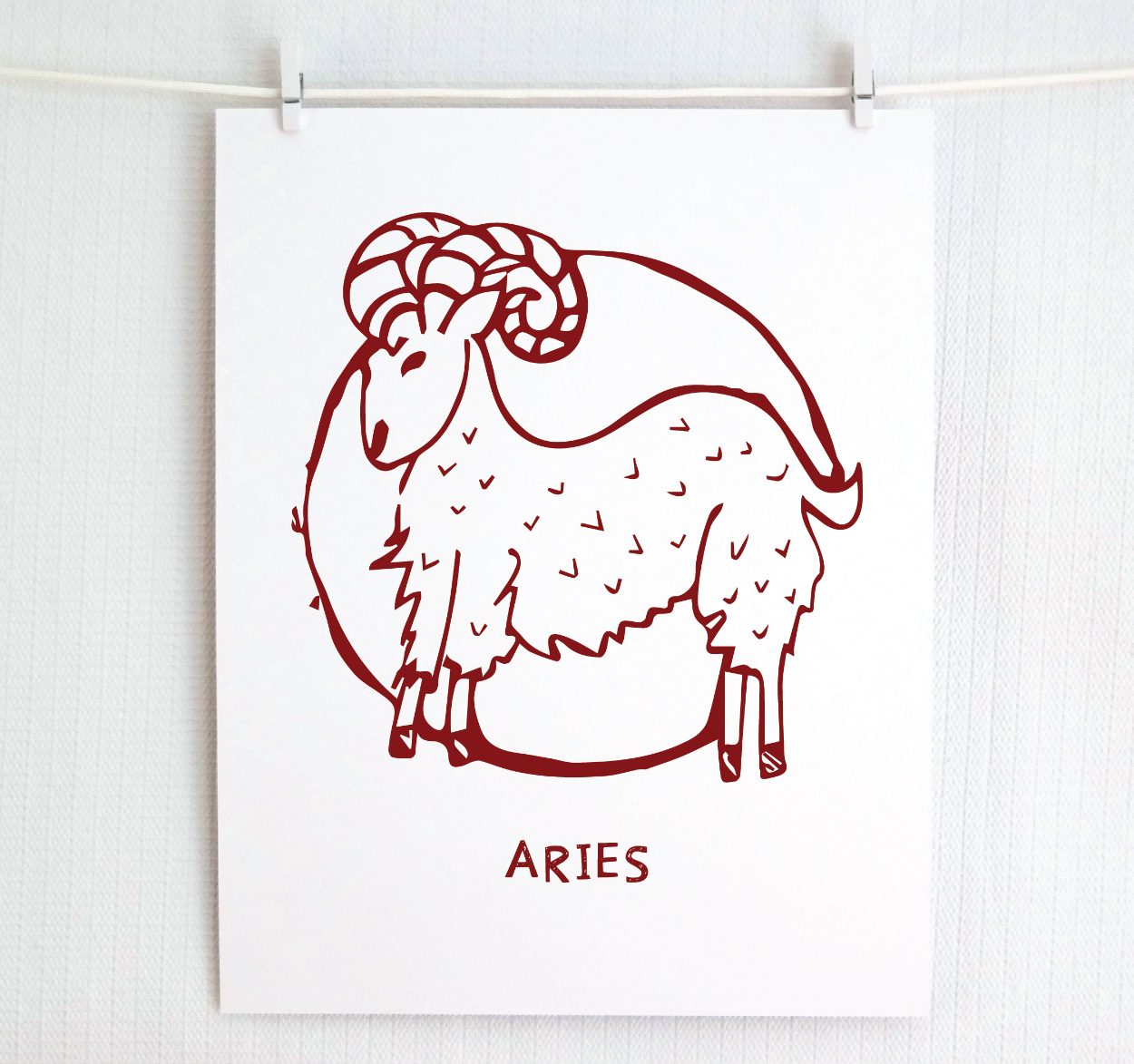 An illustration of the ARIES Zodiac sign as a ram, printed on paper with the word ‘ARIES’ at the bottom in cranberry.