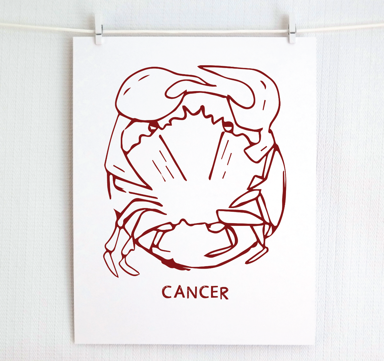 An illustration of the CANCER Zodiac sign as a crab, printed on paper with the word ‘CANCER’ at the bottom in cranberry.