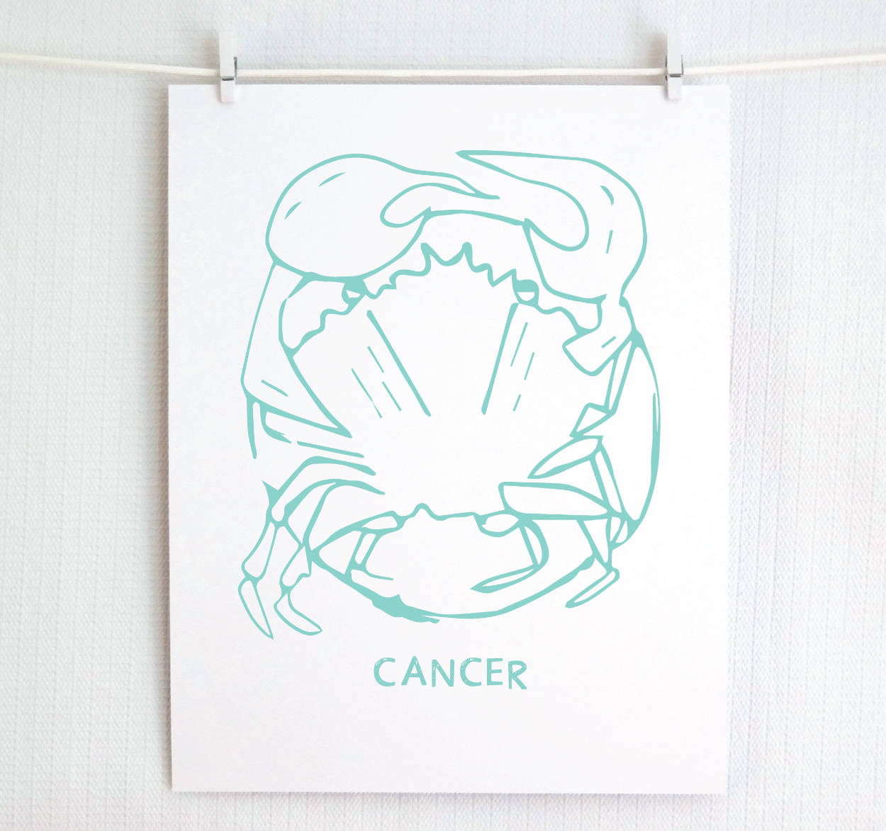 An illustration of the CANCER Zodiac sign as a crab, printed on paper with the word ‘CANCER’ at the bottom in teal.