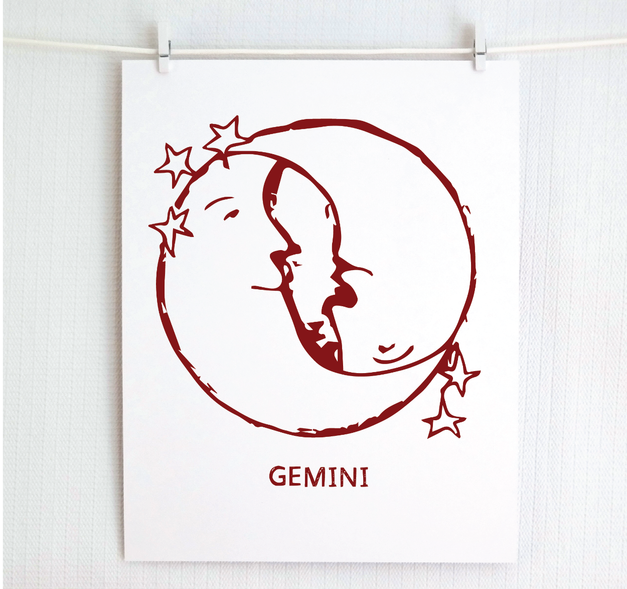 An illustration of the GEMINI Zodiac sign as crescent moons, printed on paper with the word 'GEMINI’ at the bottom in cranberry.