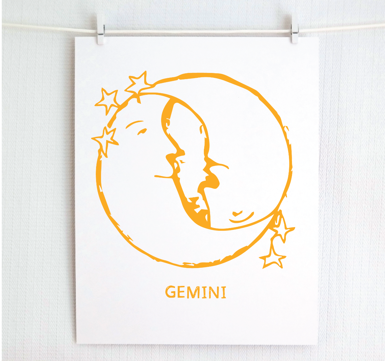 An illustration of the GEMINI Zodiac sign as crescent moons, printed on paper with the word 'GEMINI’ at the bottom gold.