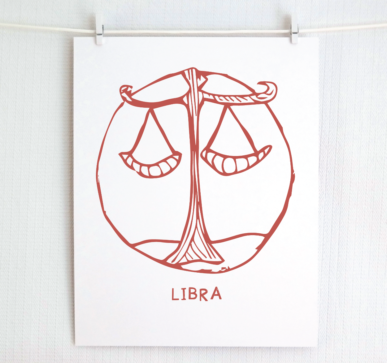 An illustration of the LIBRA Zodiac sign, printed on paper with the word 'LIBRA’ at the bottom in blush.