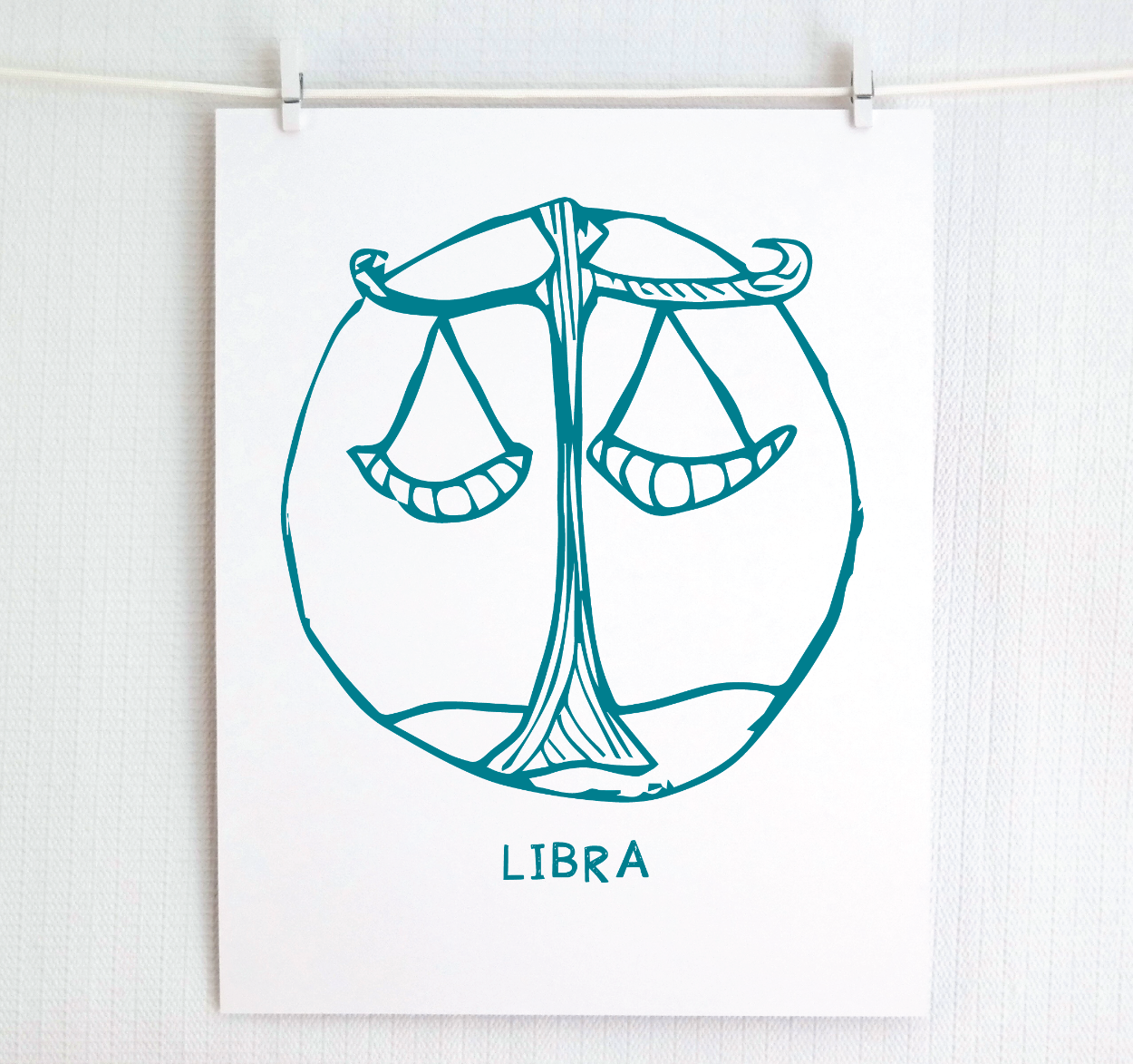 An illustration of the LIBRA Zodiac sign, printed on paper with the word 'LIBRA’ at the bottom in dark teal.