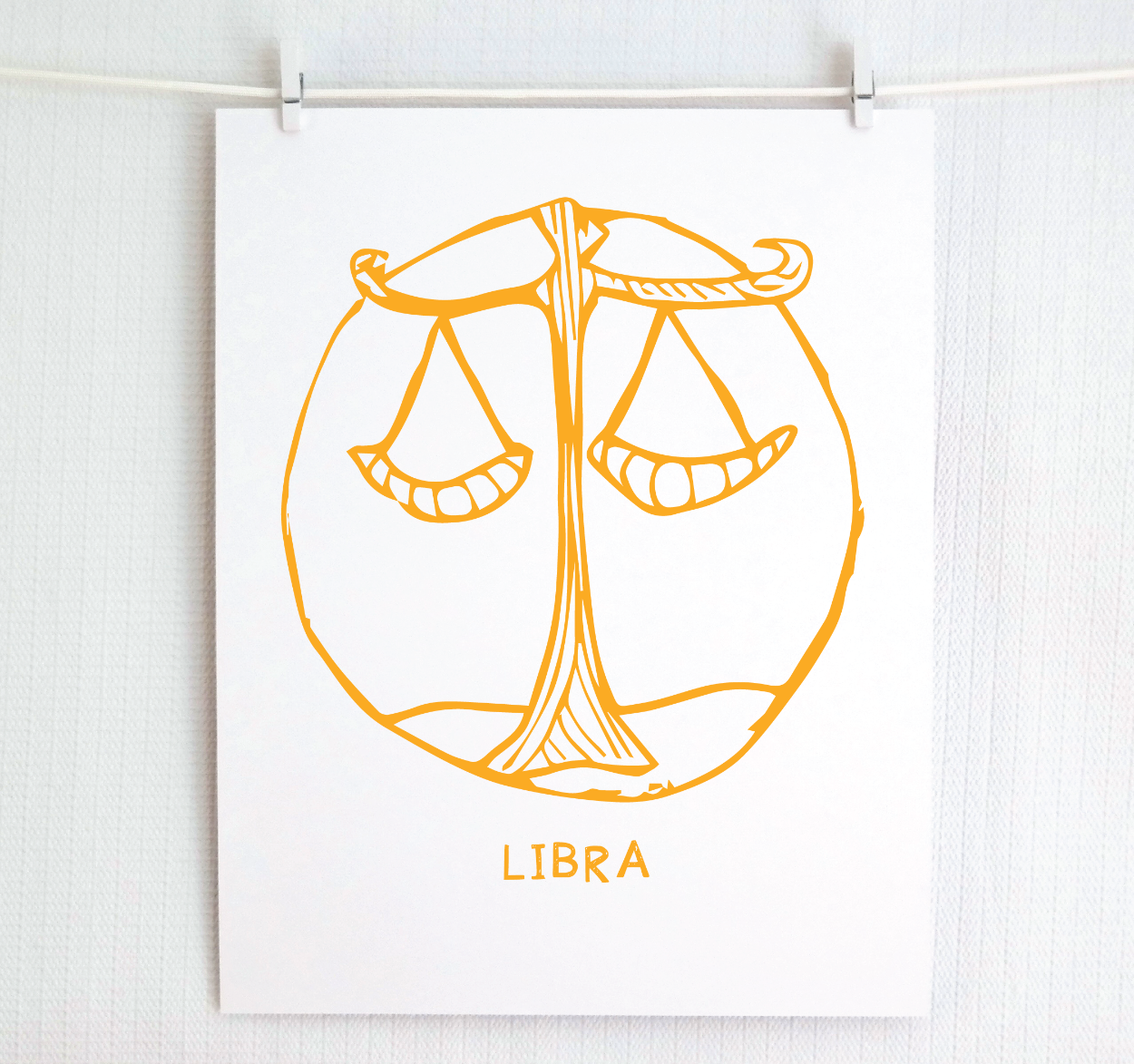 An illustration of the LIBRA Zodiac sign, printed on paper with the word 'LIBRA’ at the bottom in gold.