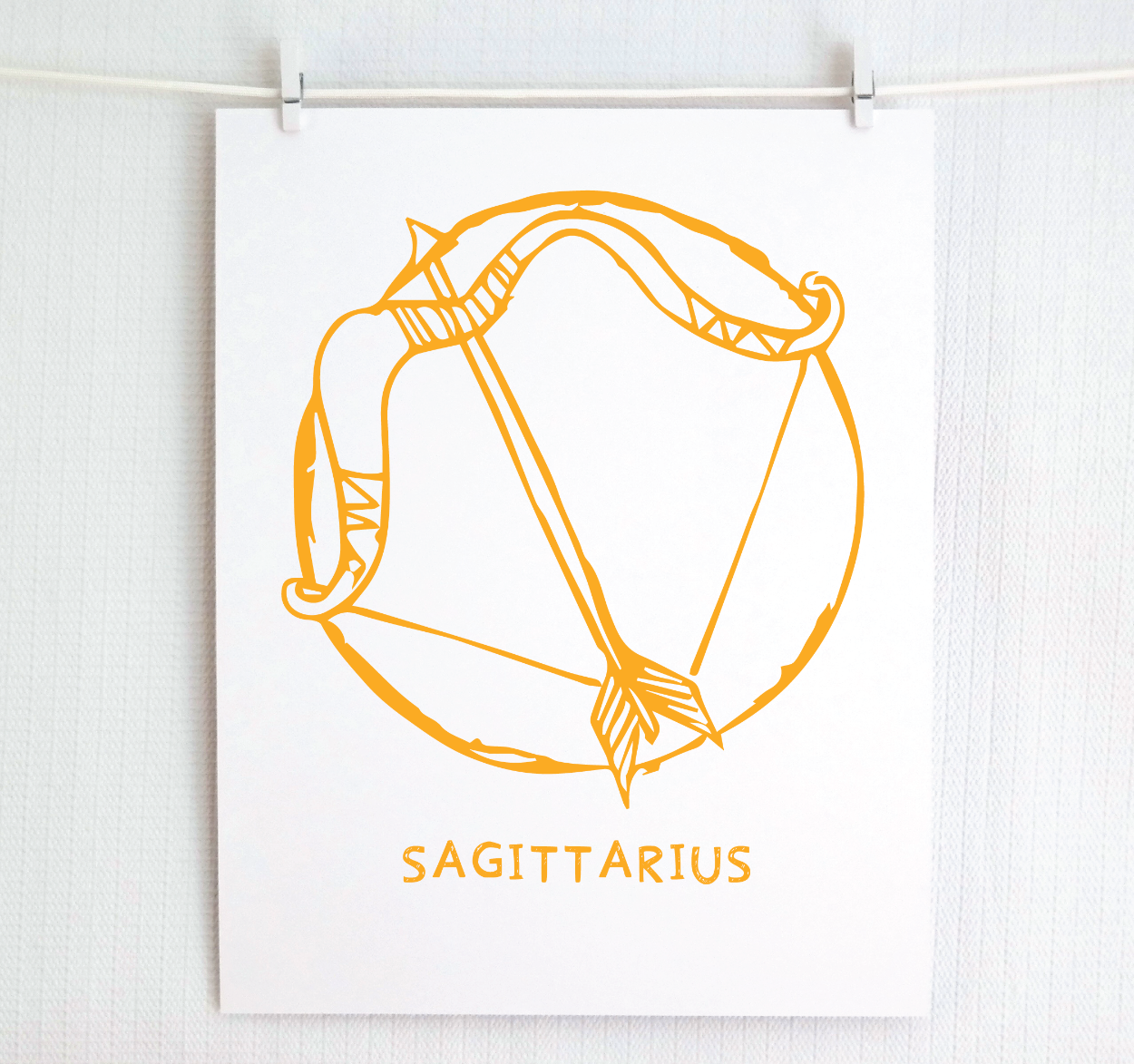 An illustration of the SAGITTARIUS Zodiac sign as a bow and arrow, printed on paper with the word ‘SAGITTARIUS’ at the bottom in gold.