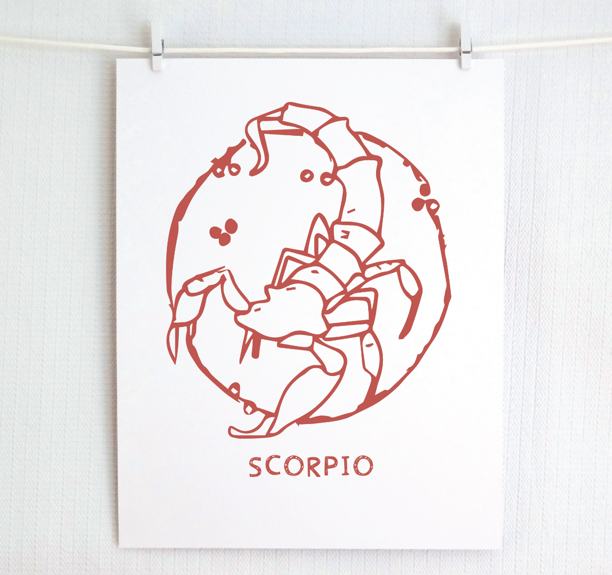 An illustration of the SCORPIO Zodiac sign as a scorpion, printed on paper with the word ‘SCORPIO’ at the bottom in blush.