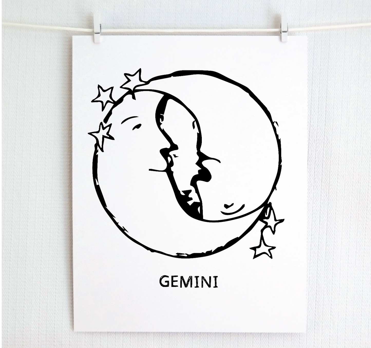 An illustration of the GEMINI Zodiac sign as crescent moons, printed on paper with the word 'GEMINI’ at the bottom.
