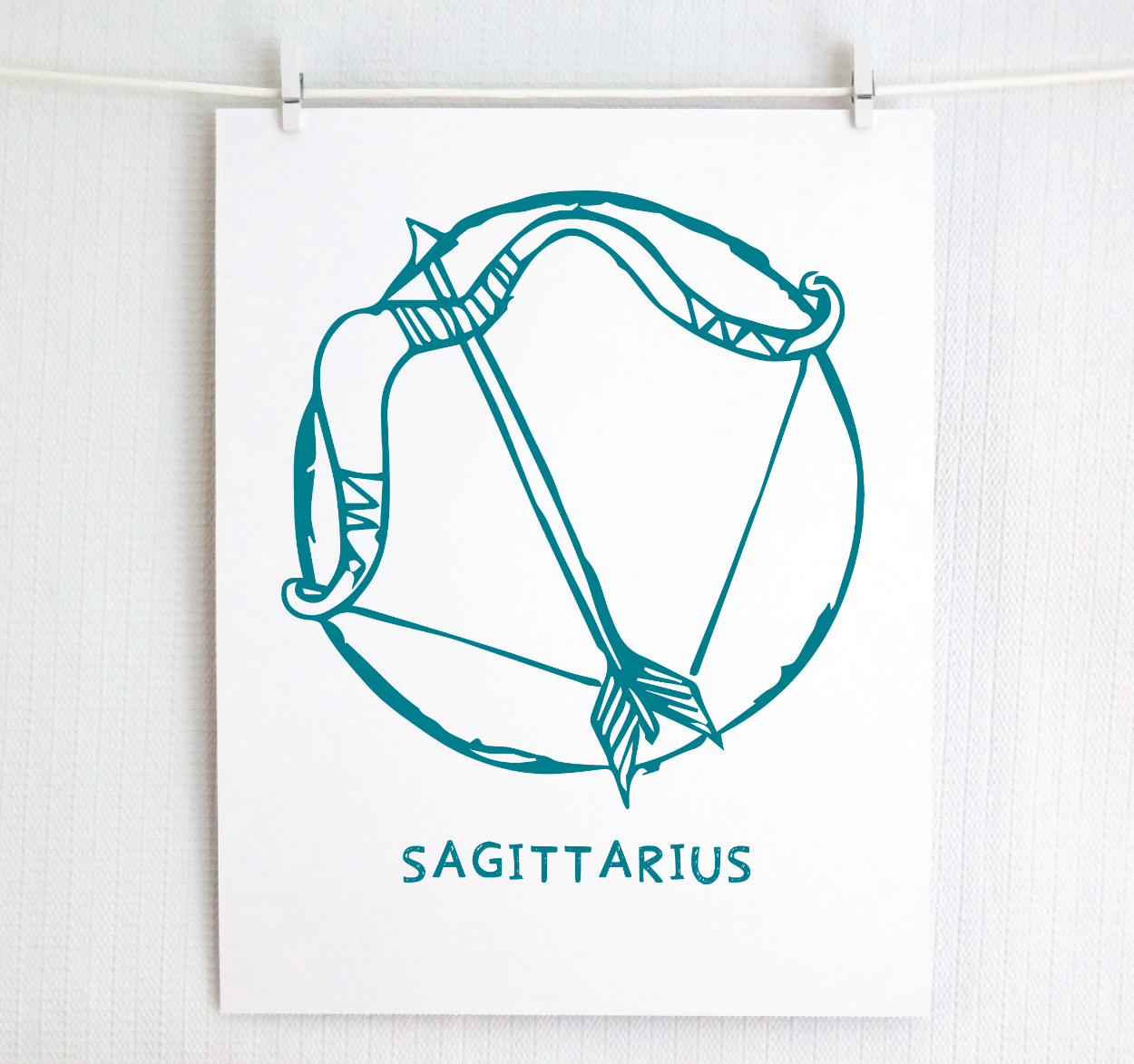 An illustration of the SAGITTARIUS Zodiac sign as a bow and arrow, printed on paper with the word ‘SAGITTARIUS’ at the bottom in dark teal.