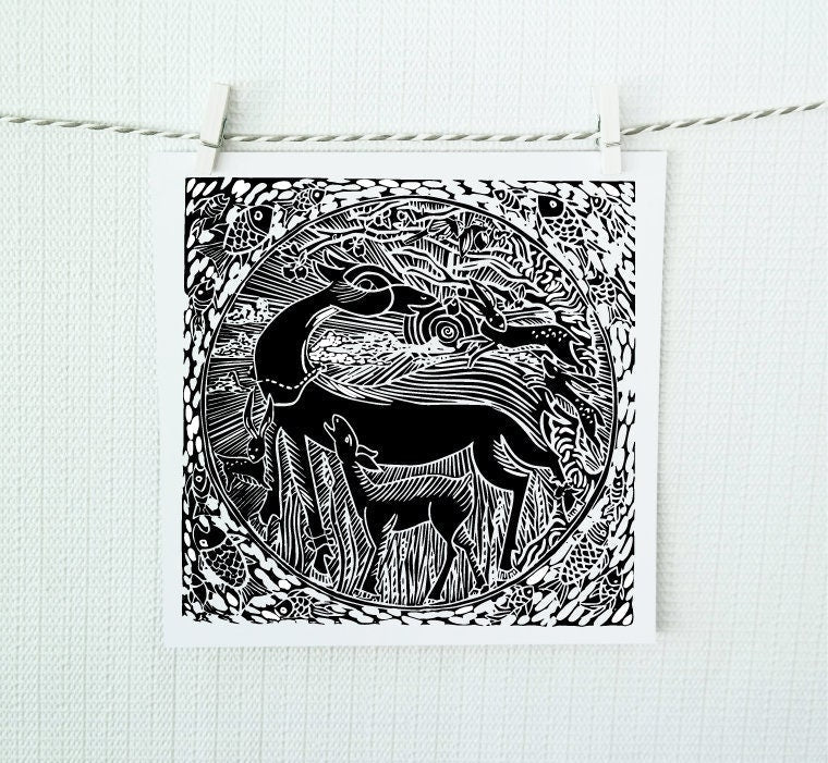 A black and white image of a hand-cut linoleum block print featuring a circular design with birds, deer, and other elements, hung on a white wall.