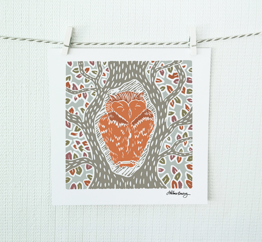 A colorful illustrated art print of an owl sitting in a tree, displayed on a wall.